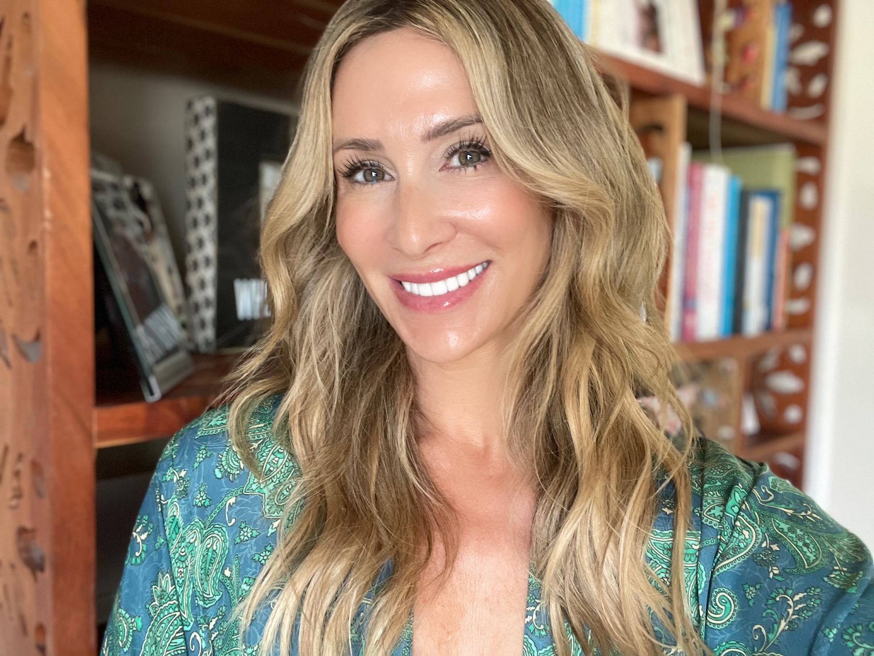 Dustine Rey smiling in front of a wooden bookshelf filled with books.